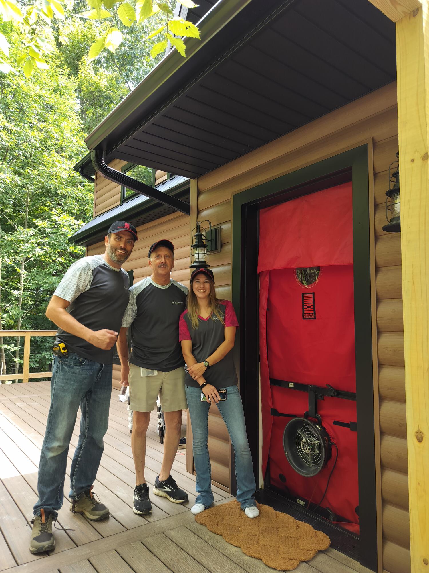 Three Harmony Home Energy team members beside a blower-door test setup on a home’s porch